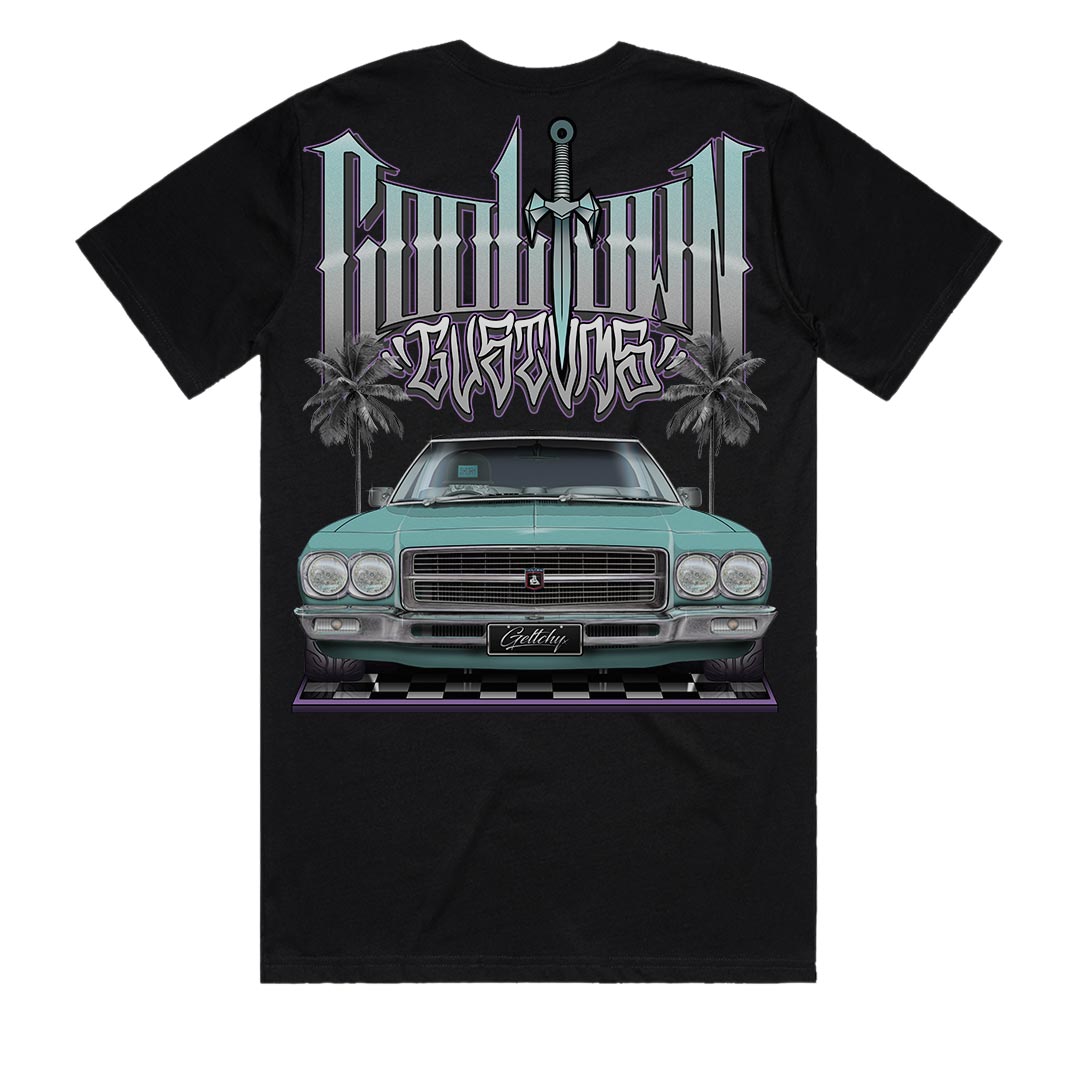 Premium black t-shirt featuring hand-illustrated Holden HQ Monaro LS in Taormina Blue, created by Australian automotive artist Mark Geltch. The design shows a front view of the classic muscle car positioned on a polished checker floor with tropical palm trees and Cooltown Customs typography in the background. The oversized 60cm back print showcases detailed automotive artwork of the iconic 5.7L 350cu GMH engine Monaro.